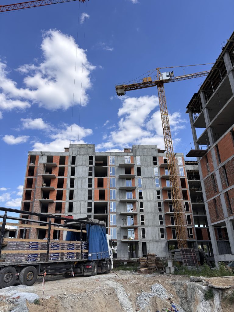 Construction site with a tall yellow crane over a partially built multi-story apartment building against a blue sky with white clouds.