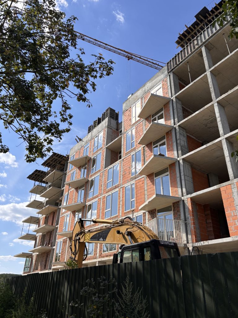Under-construction multi-storey apartment building with a crane overhead against a blue sky.